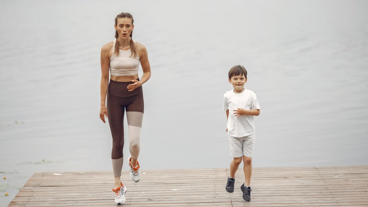 A woman and young boy jogging together on a wooden pier by a tranquil lake, enjoying leisure time outdoors.